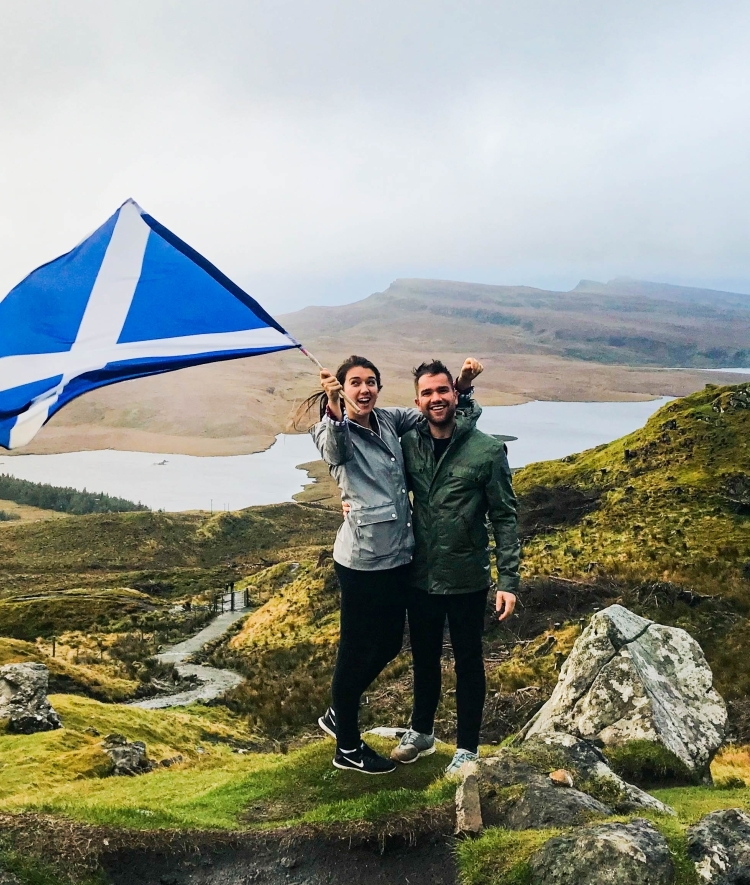 Two students wave a flag standing on green hillside