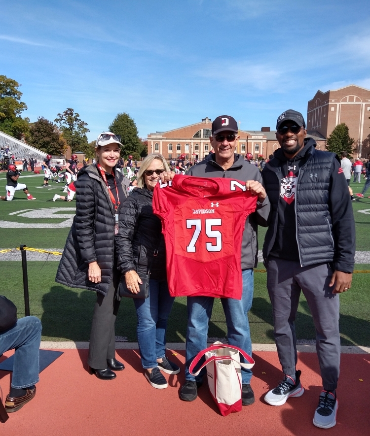 Bazos and family member hold football jersey, Chris Clunie and Carol Quillen pose with them