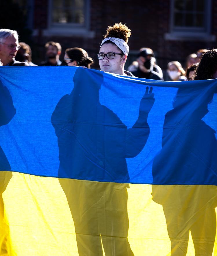 Student standing behind Ukraine flag with shadow of other students with fingers making the peace sign 