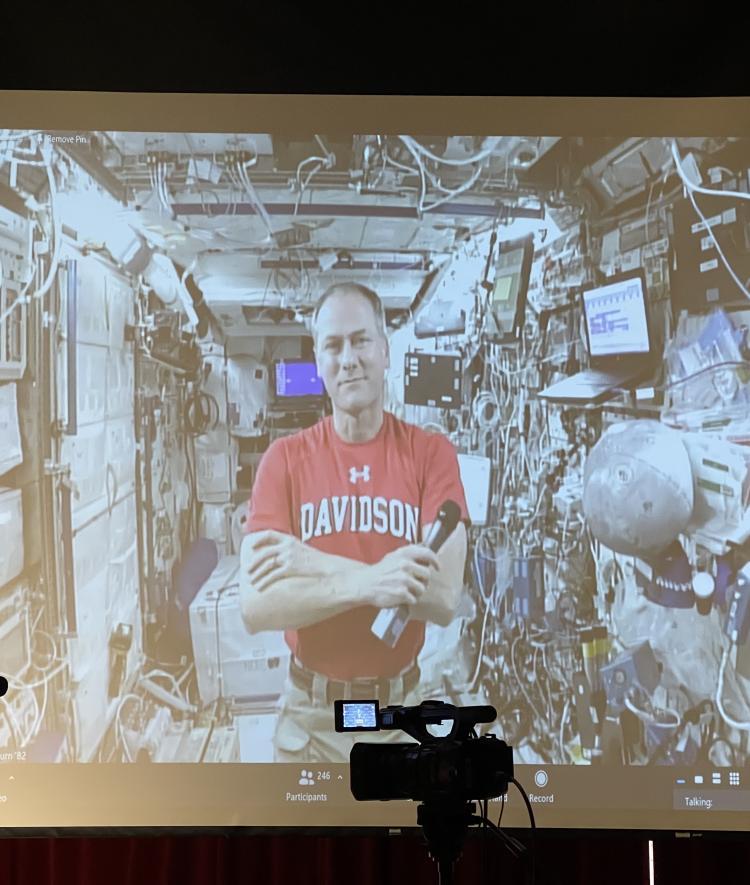 Tom Marshburn in a Davidson t-shirt on a spaceship shown on a projector screen