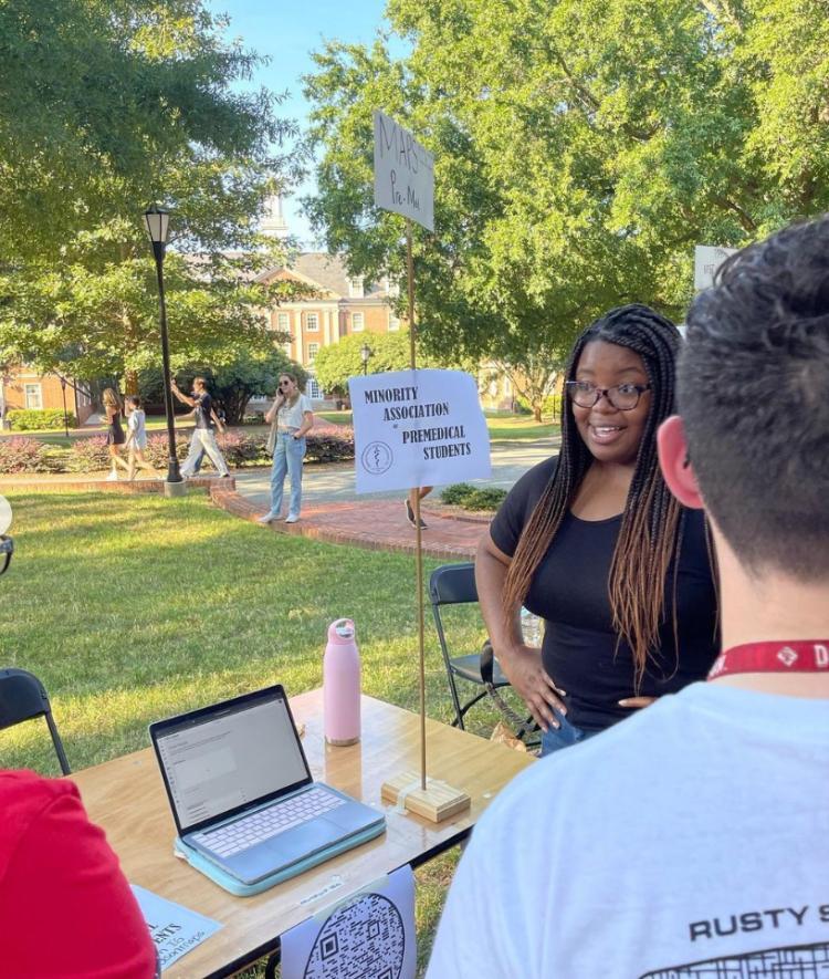black woman smiling and talking to students at table with "MAPS" sign behind her
