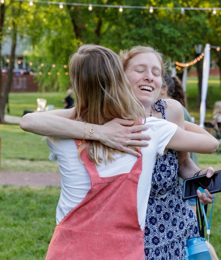 young alumni hugging with string lights in background