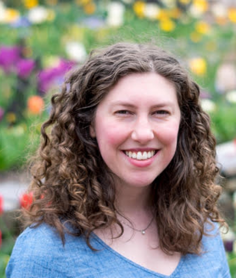 white woman with curly brown hair wearing a grey v-neck tshirt