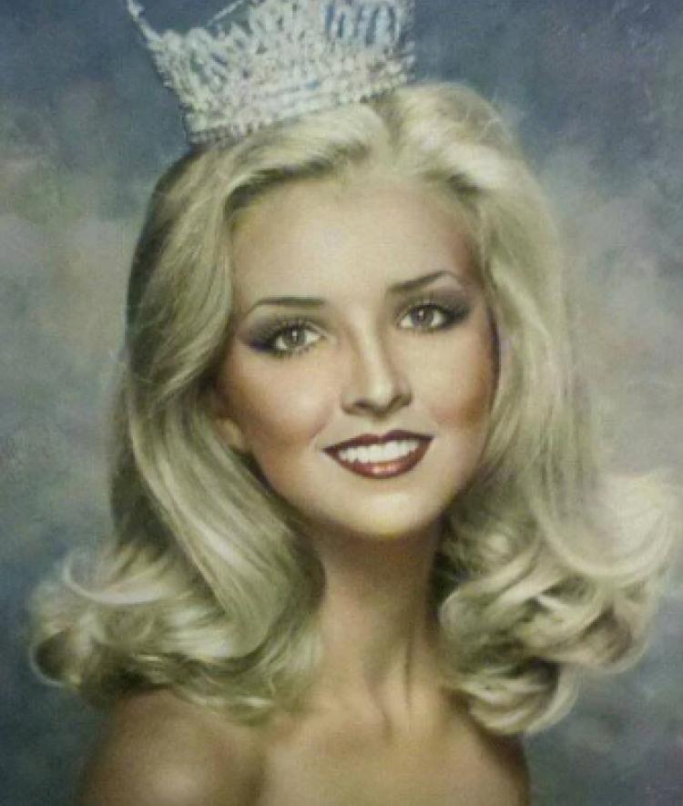 A blonde woman wears a strapless sparkly dress and a tiara on her head.