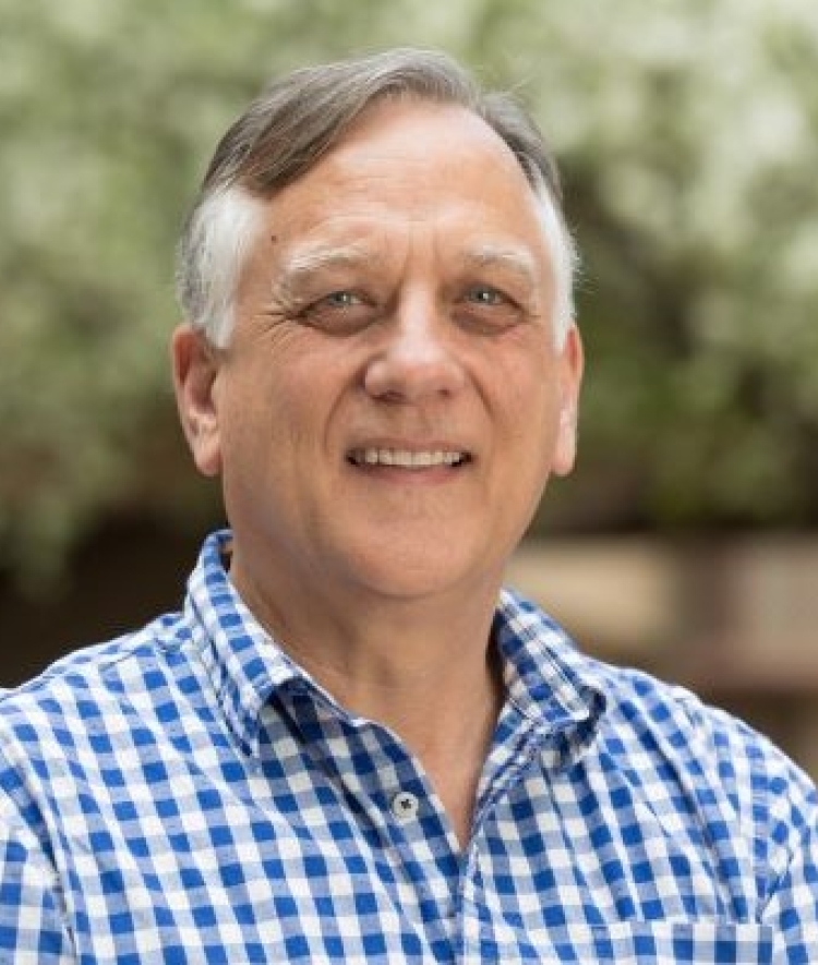 A white man wearing a blue gingham shirt and smiling