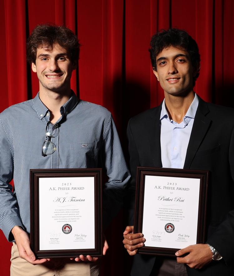 Two young men smiling and holding awards in front of a red curtain