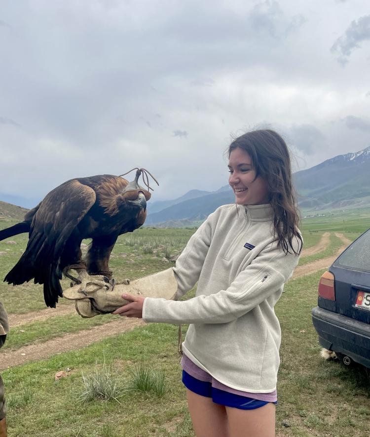 a young woman holds a falcon with mountains in the background