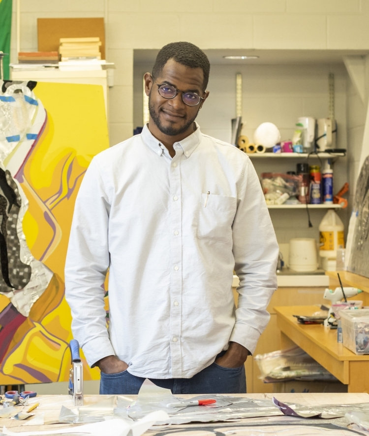 a young Black man with a white collared shirt standing in an art studio