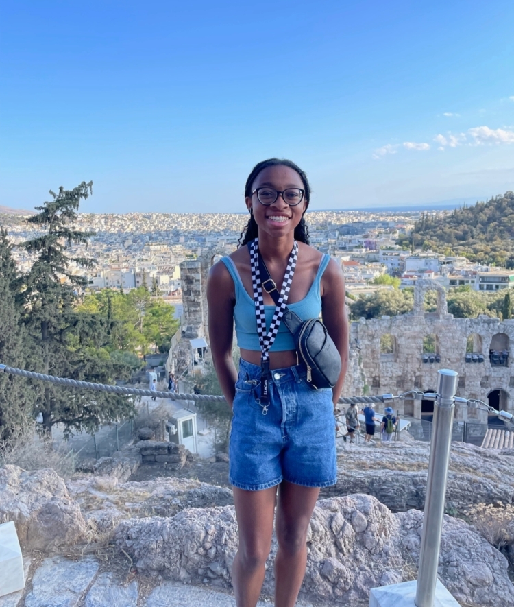 a young Black woman smiles in front of ancient ruins on a sunny day