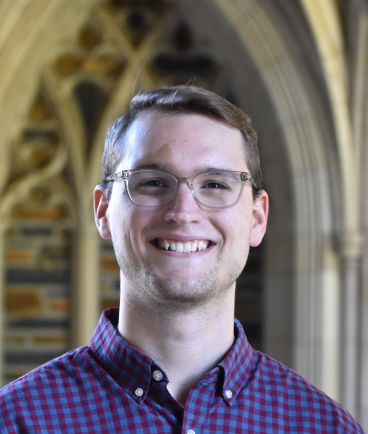 a young white man standing in front of a brick wall