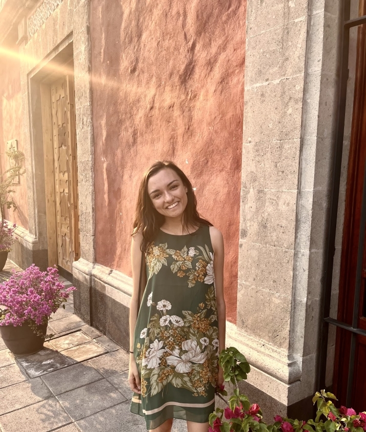 a young woman wearing a floral dress standing in front of a stone wall