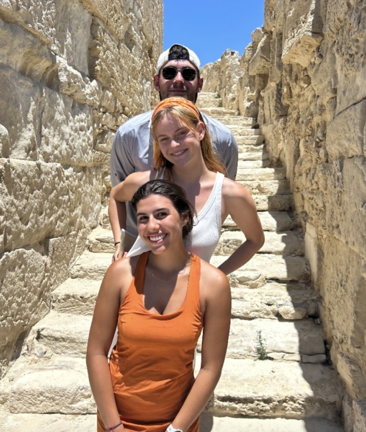 a group of three students standing on a set of stairs on an archaelogical dig