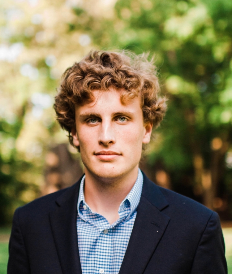 a young white male with curly brown hair wearing a collared shirt and blazer