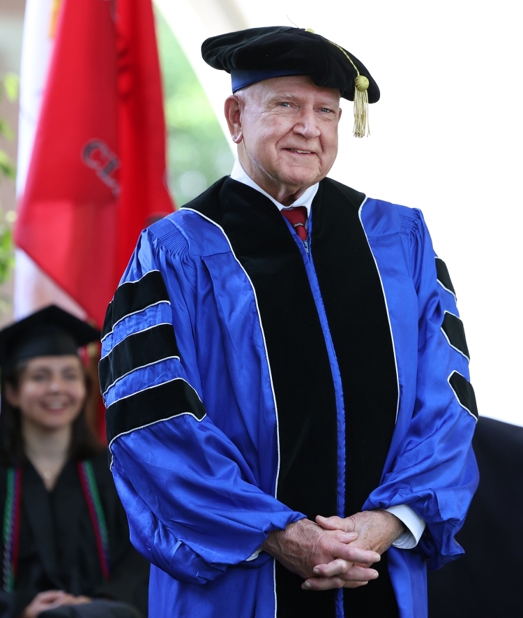 an older white man smiles while wearing graduation regalia