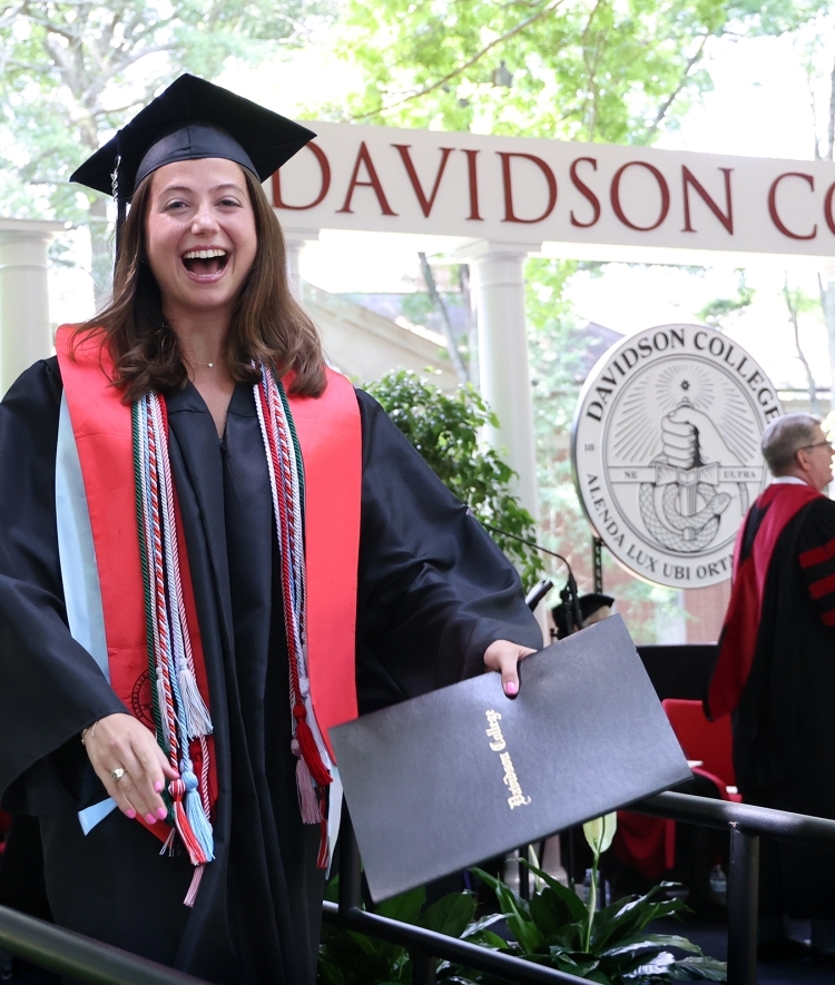 a young woman smiles in graduation robes while holding diploma