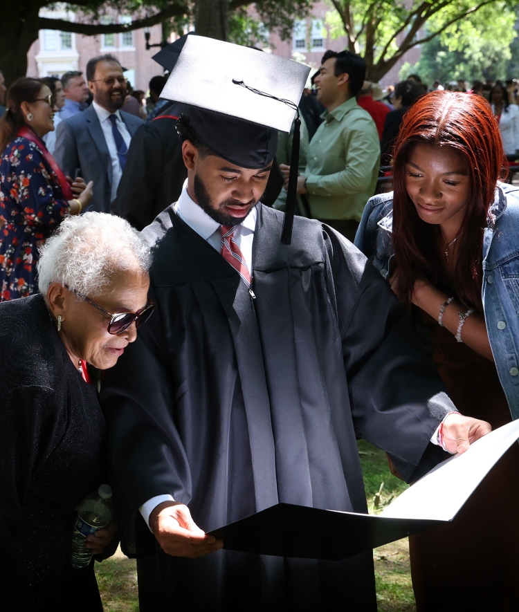 a young Black man shows his diploma to family while smiling