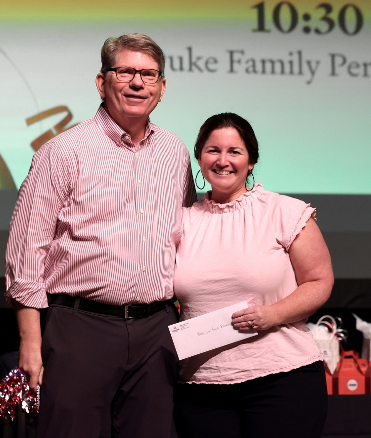an older white man and a younger white woman stand together while holding an envelope award