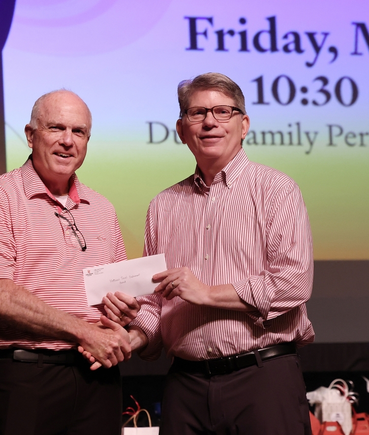 two older white men shake hands on a stage