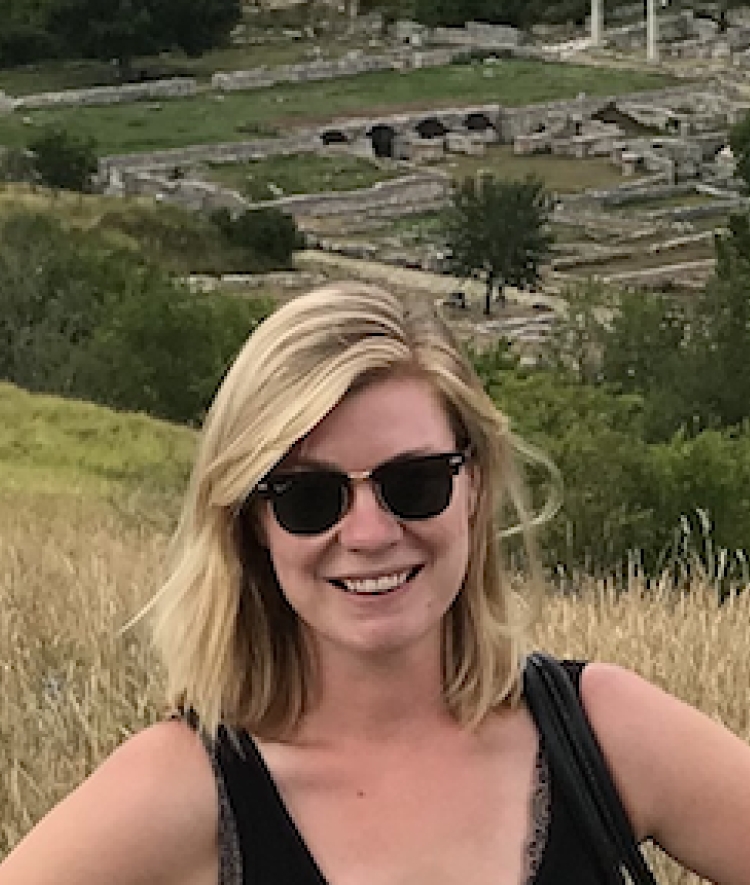 a young white woman with blonde hair wearing sunglasses standing in front of ancient ruins