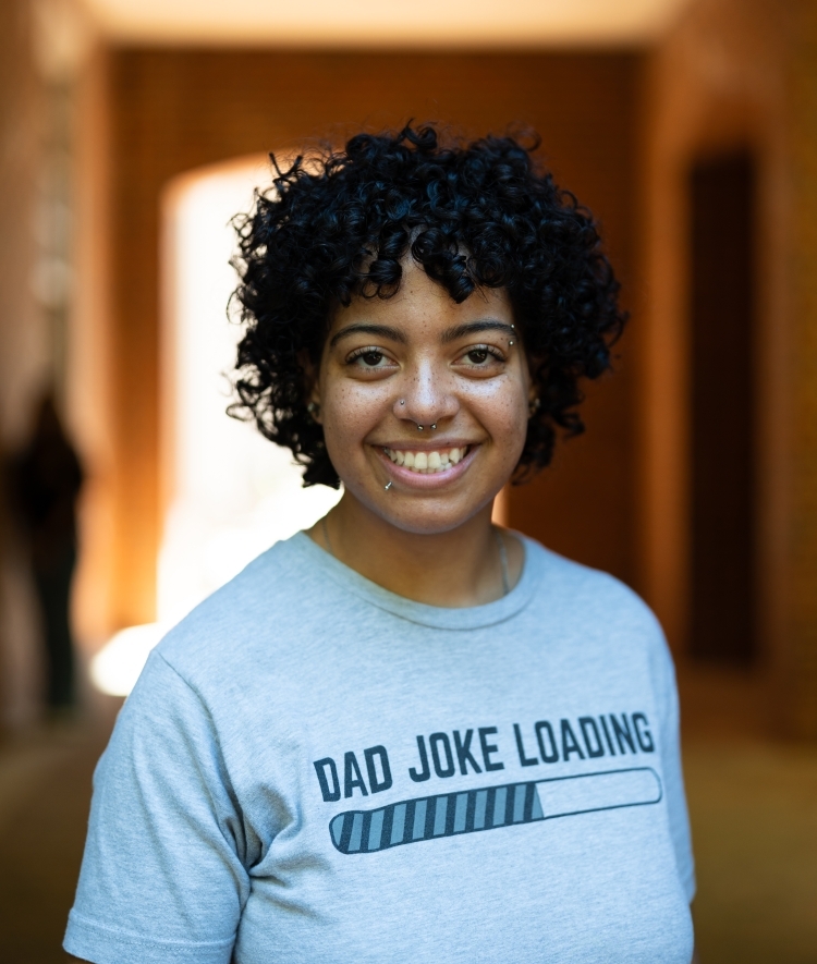 a young woman with dark curly black hair wearing a t-shirt and smiling