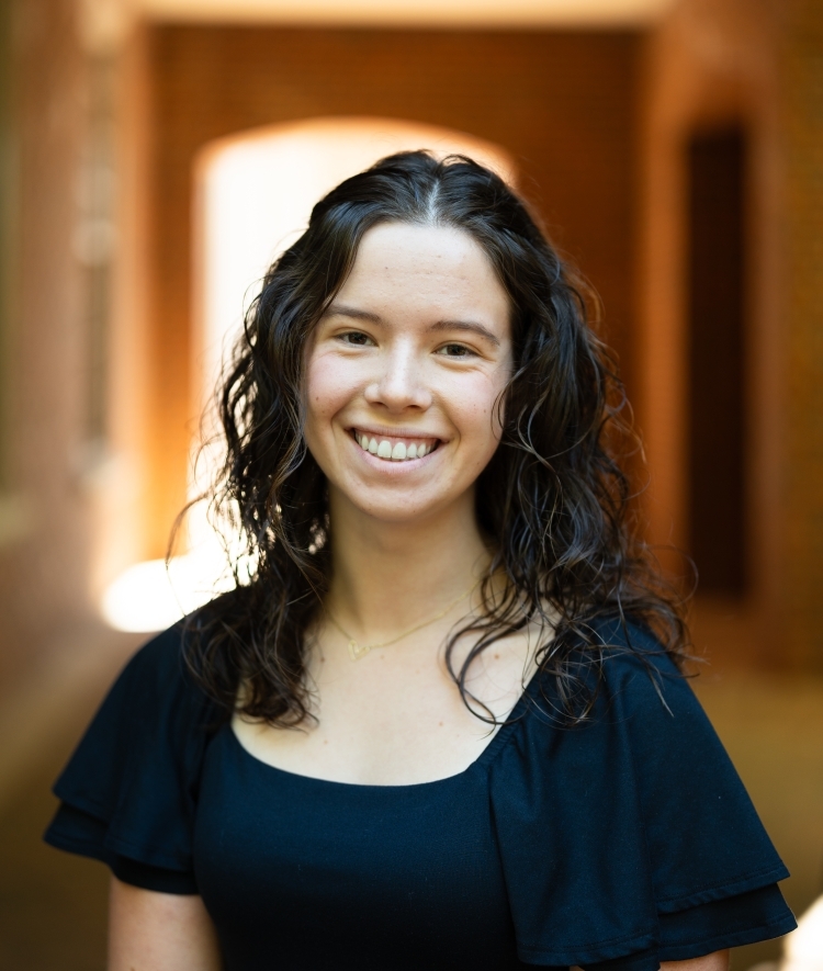 a young white woman with dark brown hair wearing a dark top and smiling