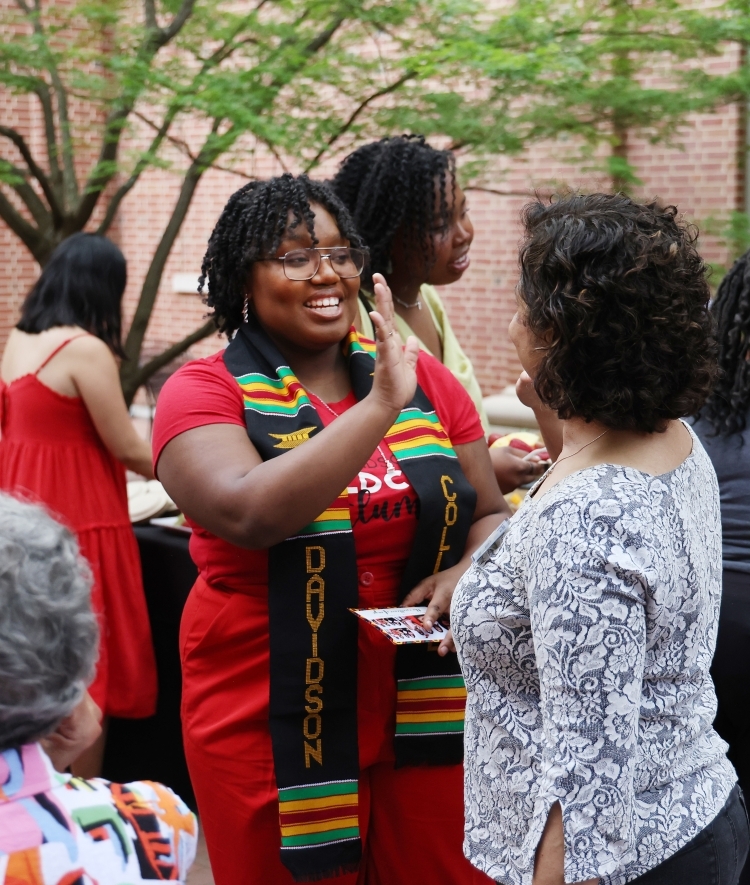 a young Black woman high fives an older woman while wearing graduation cords