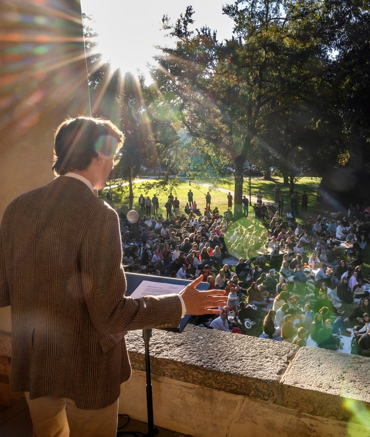 a student in a jacket speaks out over a crowd from a columned building