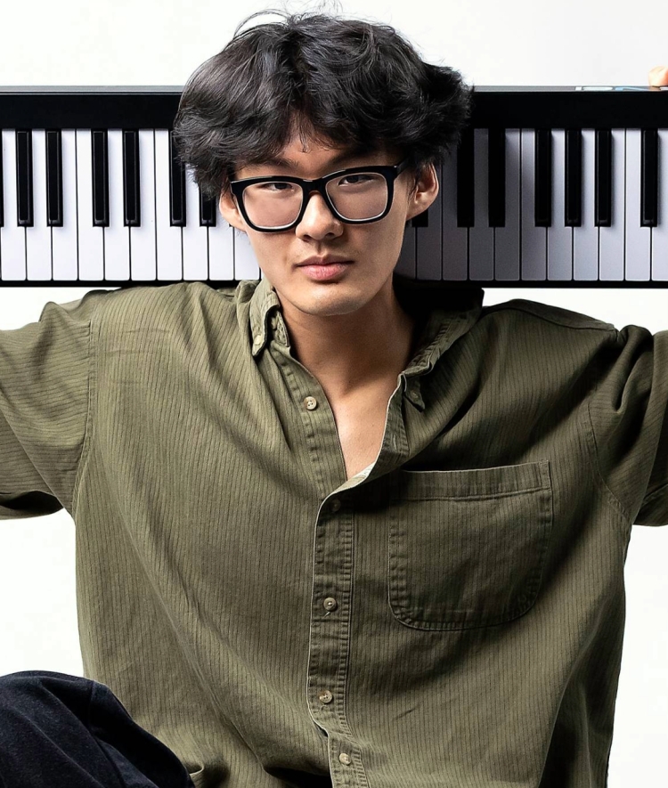 a young Asian man holding a keyboard on his back while sitting cross-legged