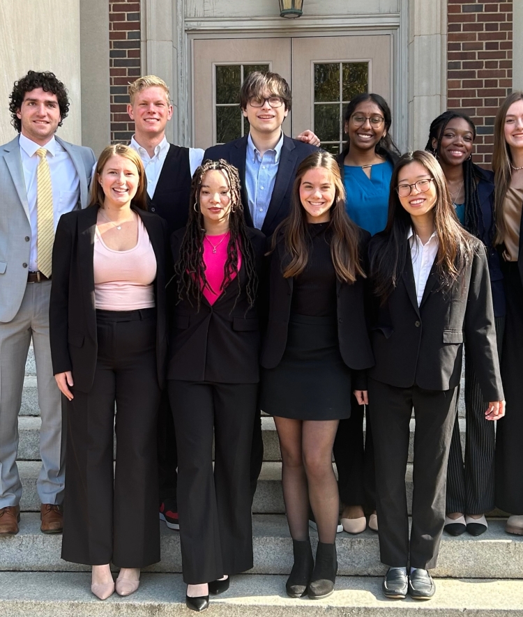 a group of young people in business formal clothing standing together in front of an academic building