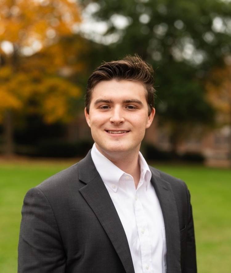 a young white man wearing a white collared shirt with a black jacket while standing outside