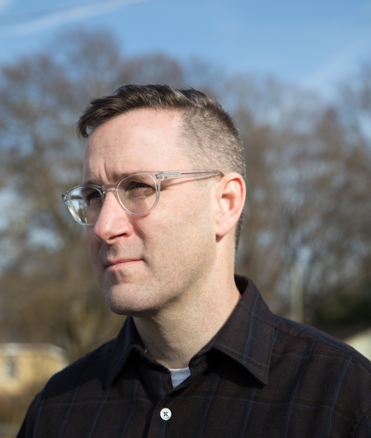 a young white man wearing glasses and a black collared shirt