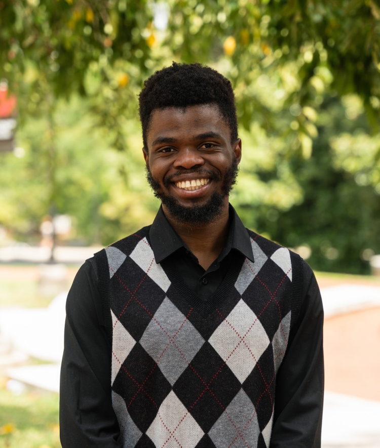 a young Black man wearing a black and grey sweater vest and smiling