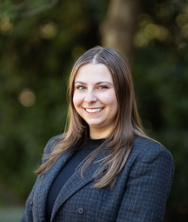 a young white woman with brown hair wearing a black blazer and standing outside