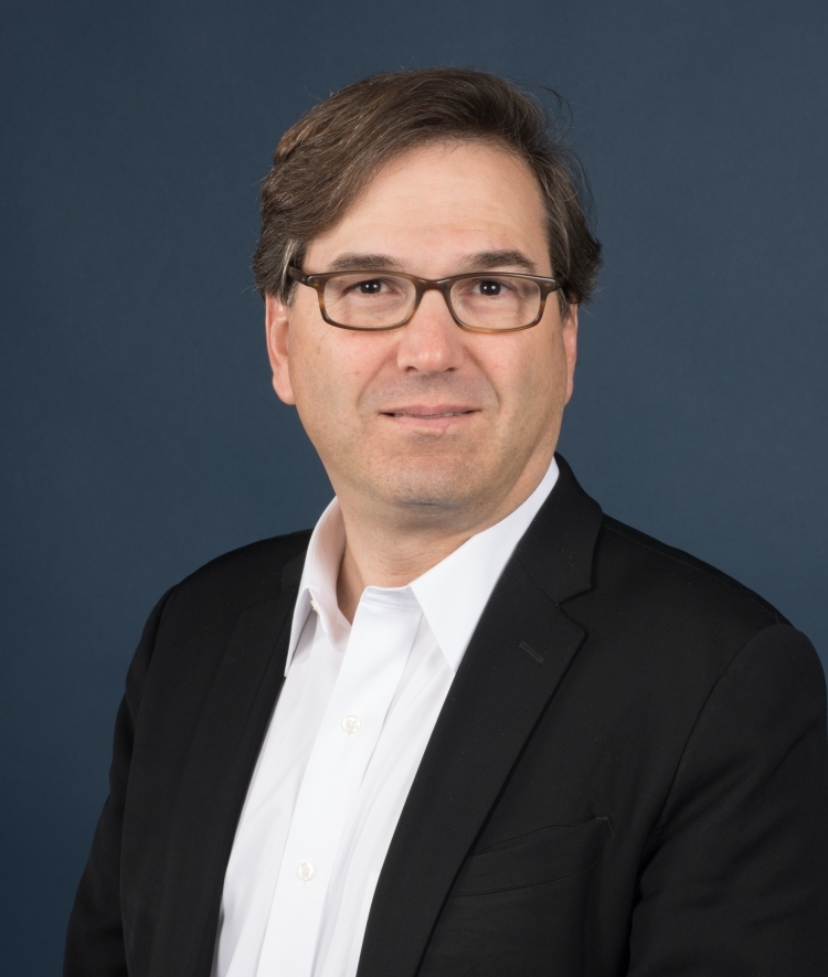 a middle aged white man wearing a white shirt, black jacket and glasses
