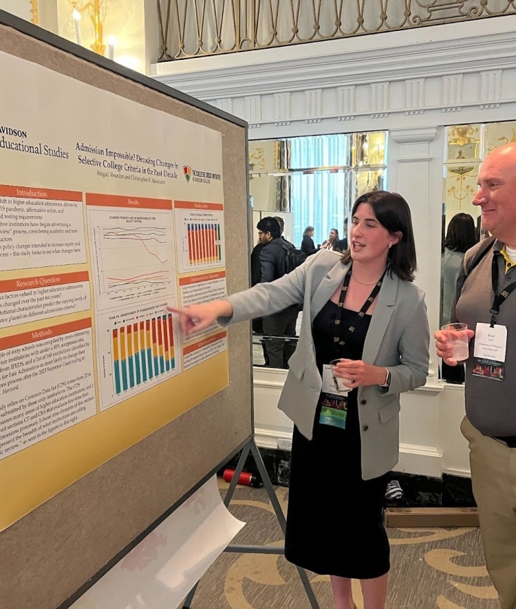 a young woman presents a poster to an older man 