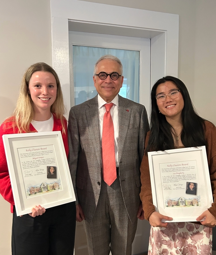 two young women hold awards with their professor