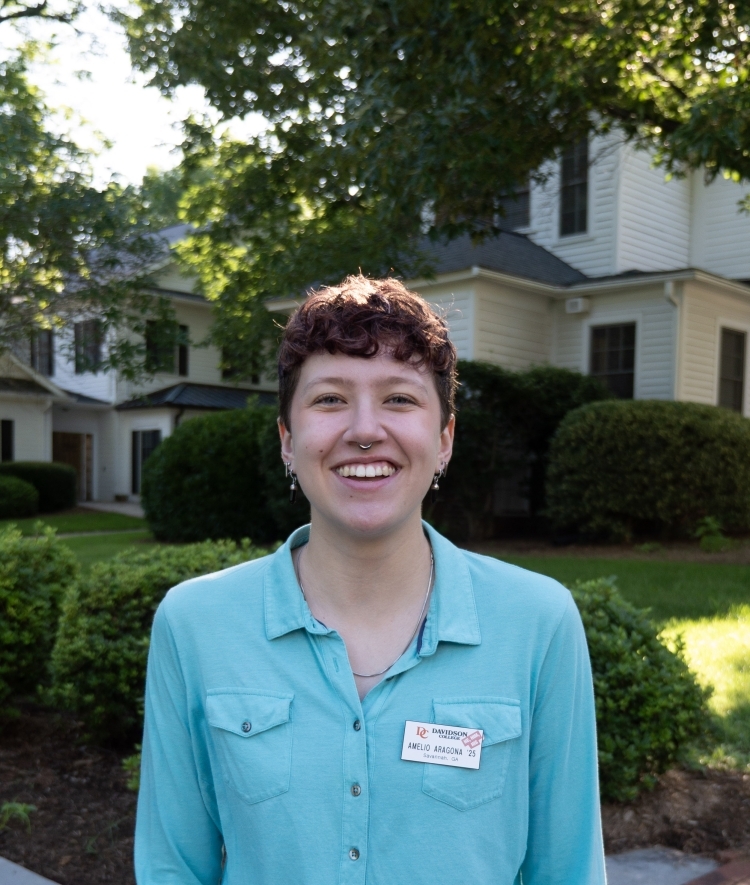a young person smiling wearing a light teal collared shirt outside on a sunny morning