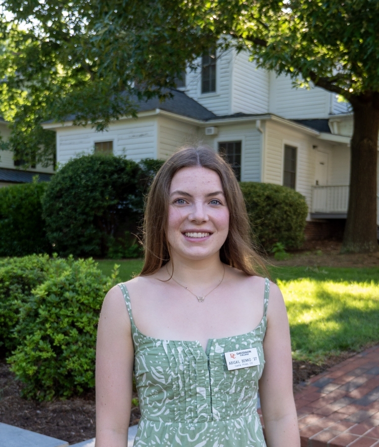 a young white woman wearing a green sundress outside on a sunny morning