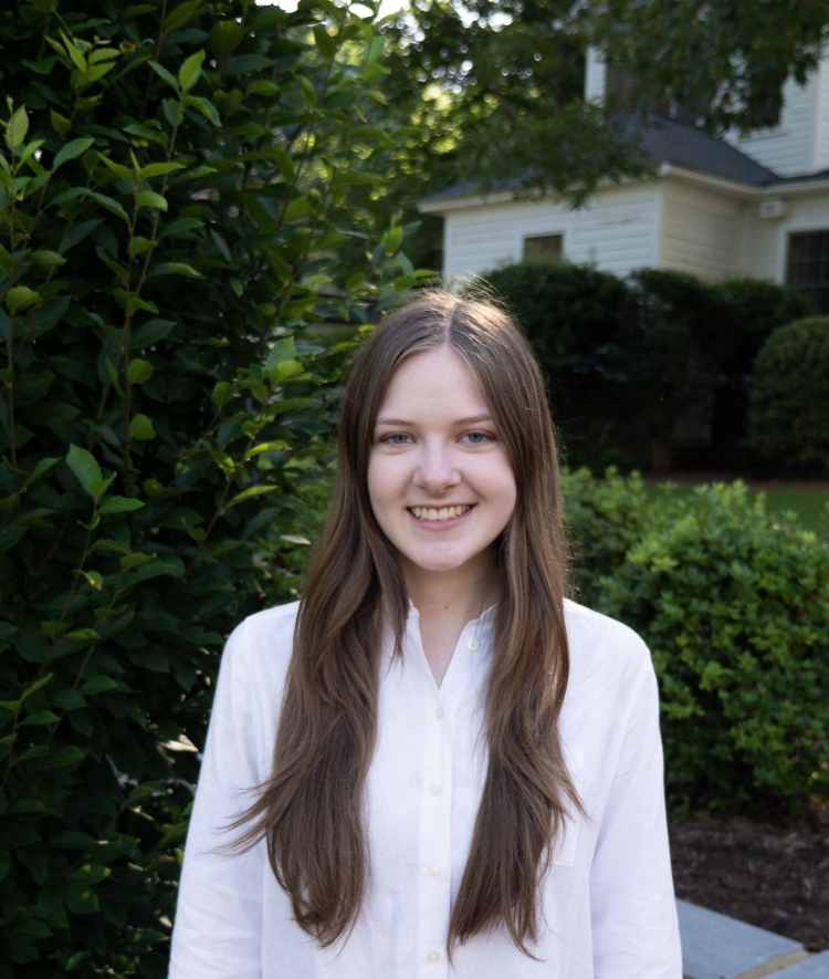 a young white woman wearing a collared white shirt outside on a sunny morning