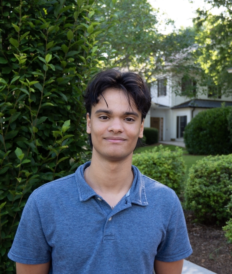 a young man with dark hair wearing a blue collared shirt on a sunny morning