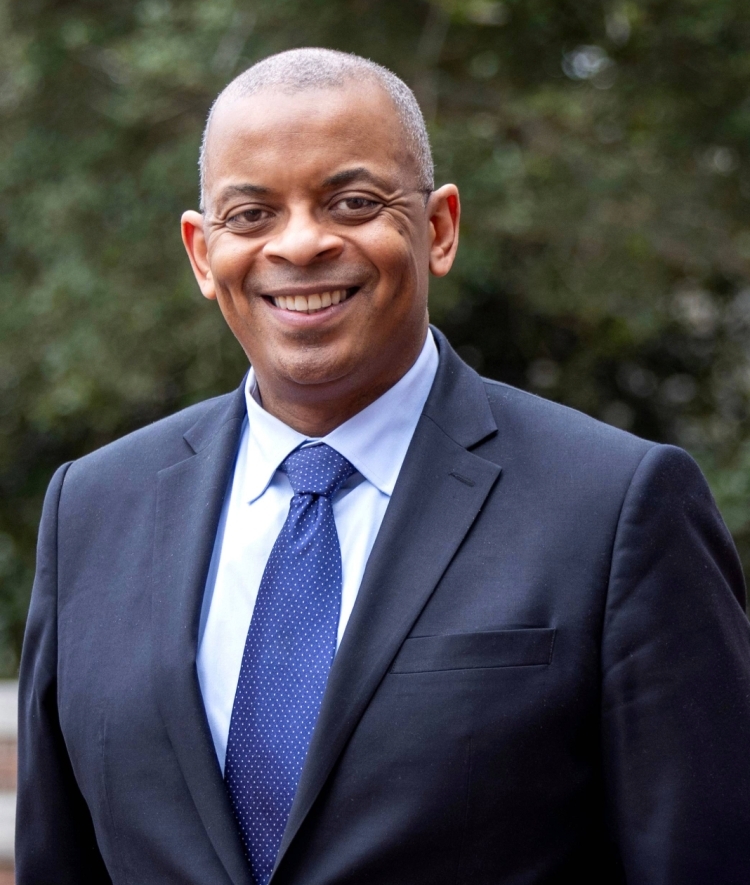 a Black man wearing a suit and tie smiling outside