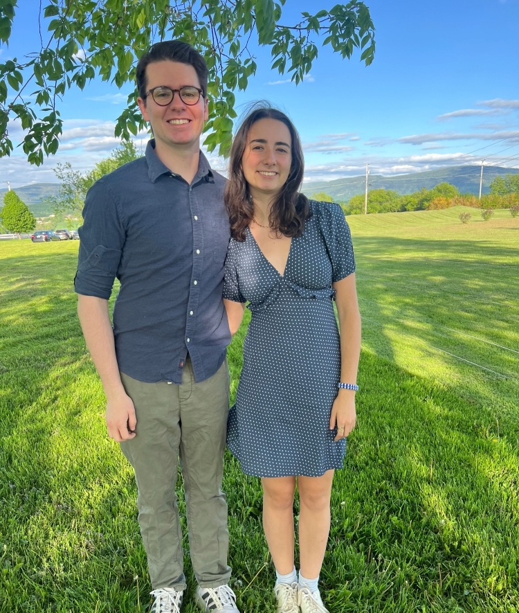 a young white woman and a young man standing in a grassy field on a sunny day