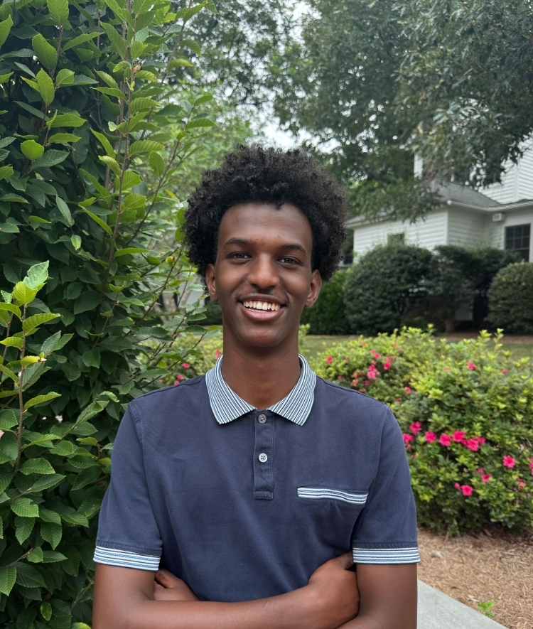 a young Black man wearing a collared shirt and smiling outside