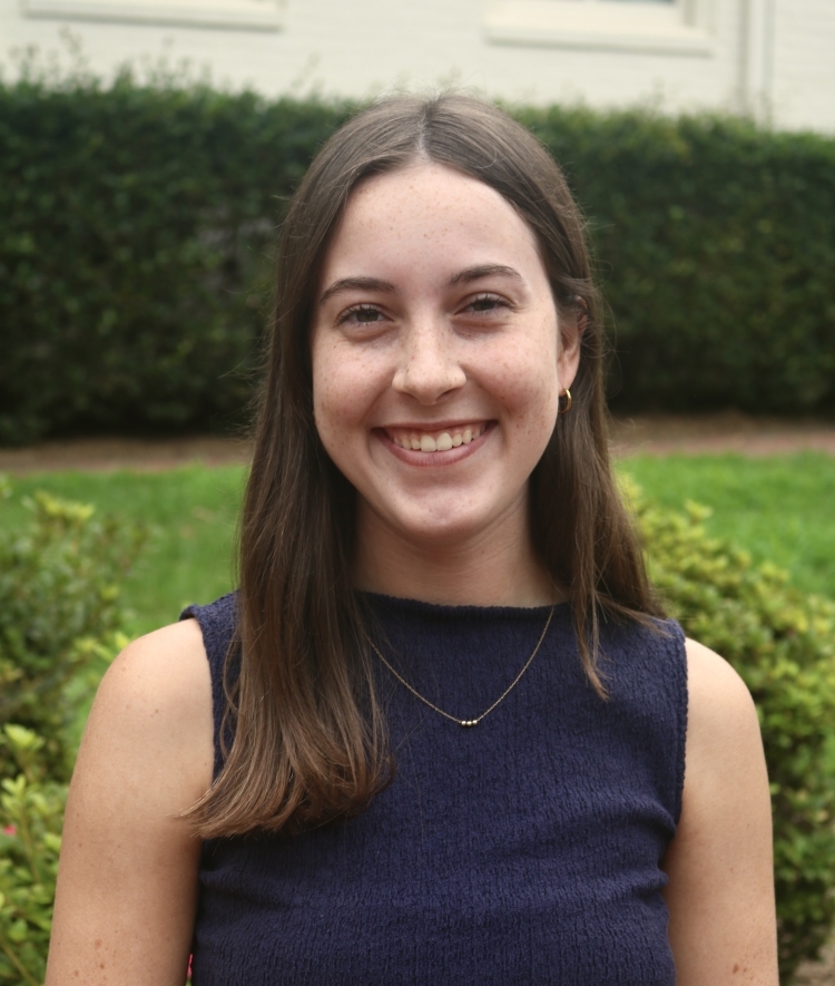 a young woman with long dark hair wearing a navy top and smiling outside