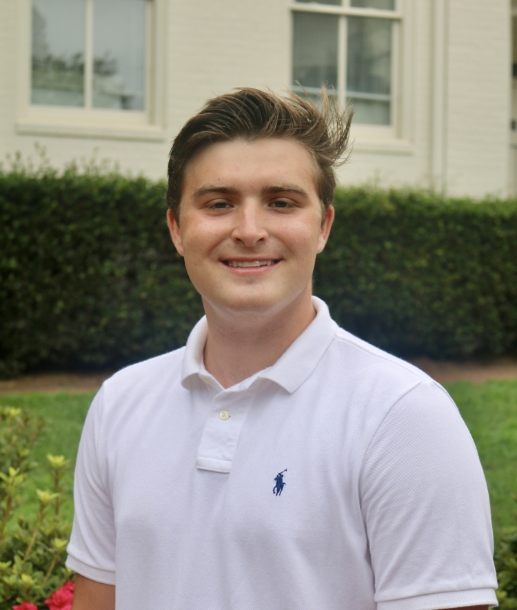 a young man with short light brown hair wearing a white polo and smiling outside