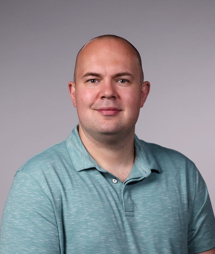 a man wearing an aqua polo smiling on a grey background