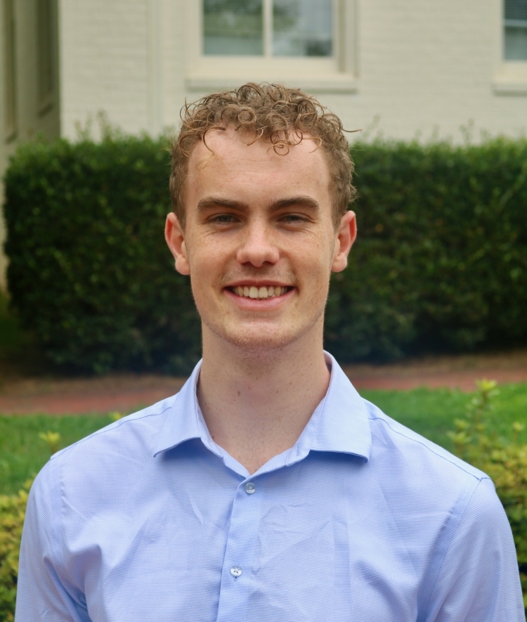 a young man with curly blonde hair wearing a blue collared dress shirt