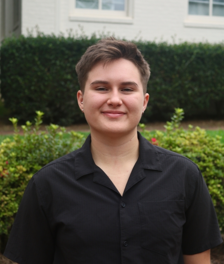 a young woman with short brown hair wearing a black collared top smiling outside
