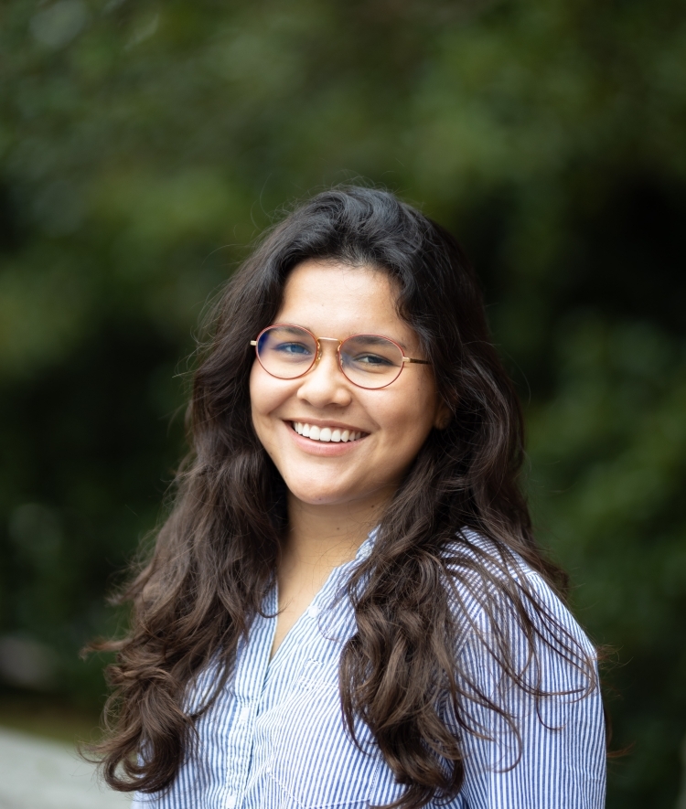 a young woman with long dark curly hair wearing glasses and a collared blue shirt