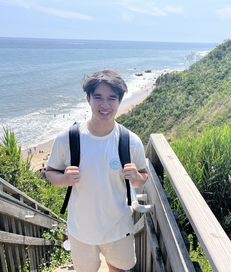 a young man wearing a backpack on a boardwalk near a beach on a sunny day